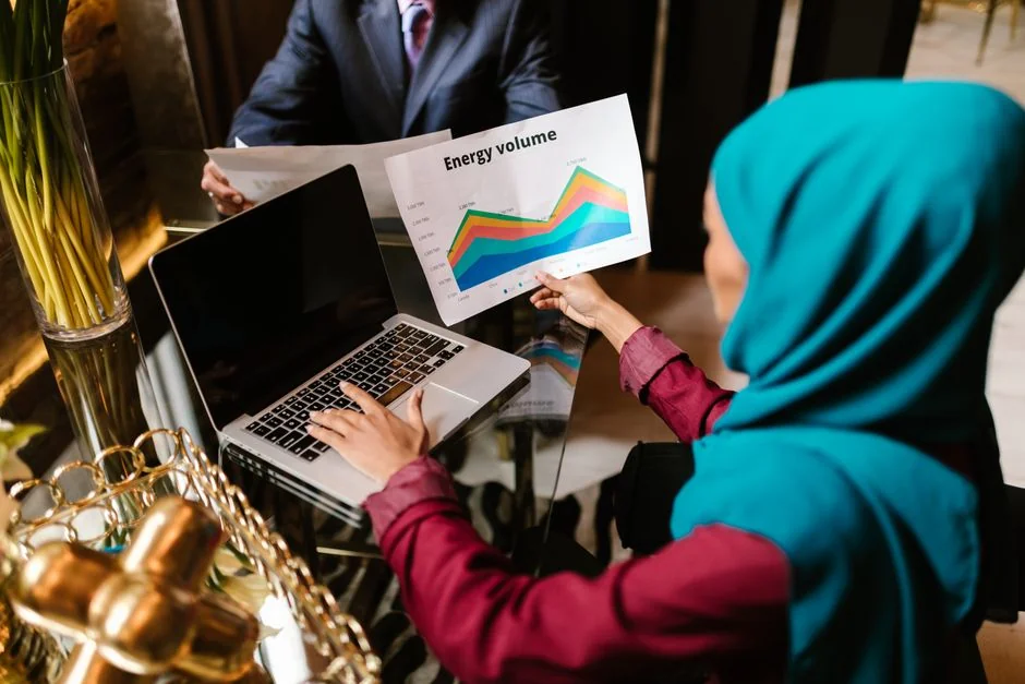 Two businessmen analyze stock market data using a smartphone and laptop in a modern office setting.
